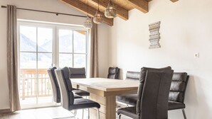 Un coin repas avec une table en bois et quatre chaises, un plafond en bois et une vue sur les montagnes grâce à de grandes fenêtres.