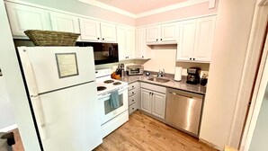 Une cuisine de taille réduite, avec des meubles blancs, un réfrigérateur, un four à micro-ondes, une cuisinière, un évier et un lave-vaisselle.