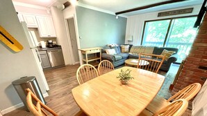 Un coin repas avec une table et des chaises en bois, une petite plante en pot, et en arrière-plan, une vue sur la cuisine et le salon.