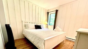 Une chambre bien rangée, avec un lit, une table de chevet et une fenêtre avec des rideaux.