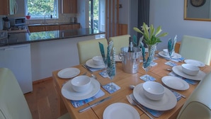 Ein Essbereich mit Holztisch, gedeckt für eine Mahlzeit, einer Küche im Hintergrund und Blick ins Freie.