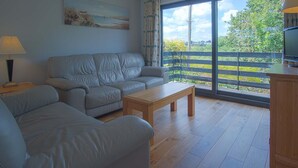 Ein Wohnzimmer mit grauem Sofa, einem Holztisch und einem Fernseher auf einer Holzkommode.