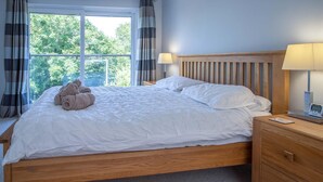 Ein ordentlich bezogenes Bett mit weißer Daunendecke, einem Holz-Kopfbrett und einem Nachttisch mit Lampe und einer Seiko-Uhr.