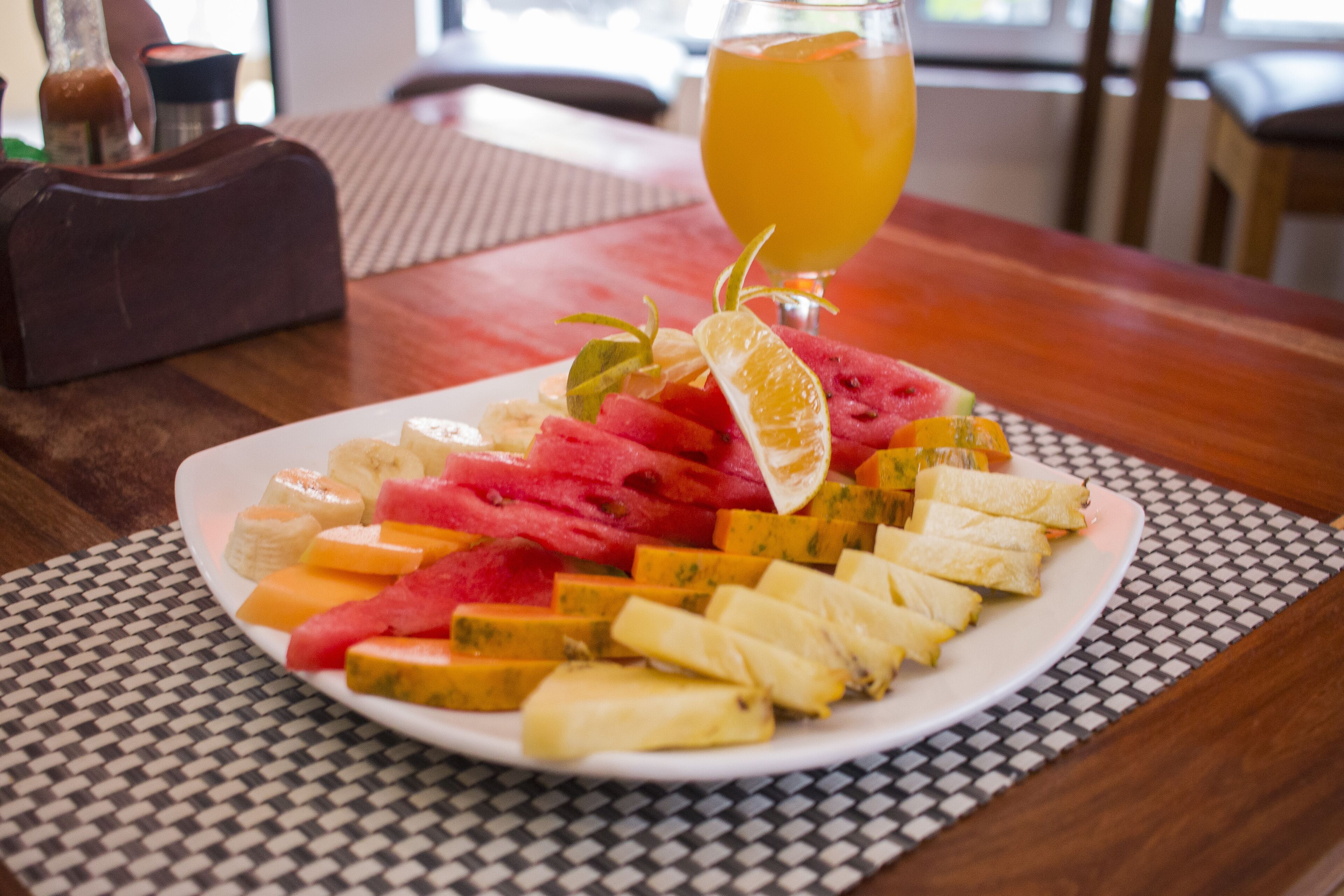 Een bord met fruit en een glas sinaasappelsap op een tafel.