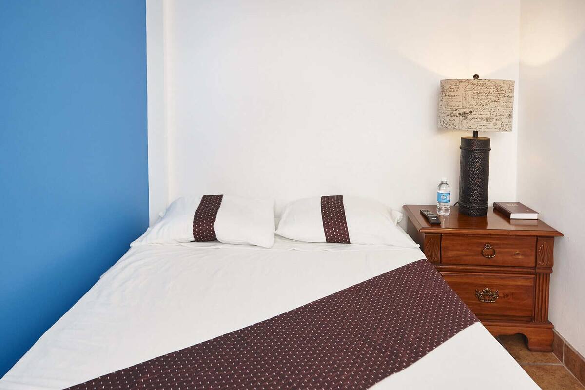 A hotel room with a bed, a nightstand, a lamp, and a water bottle.