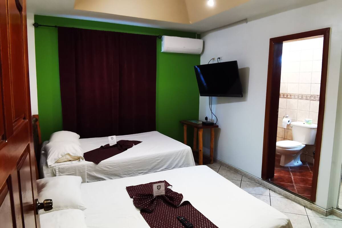 A hotel room with two beds, a television, and a bathroom visible through an open door.