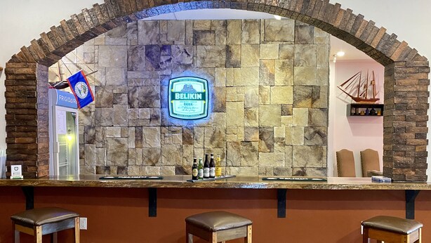 A bar area with a stone wall, a 'Belikin Beer' sign, and three wooden stools. - Hotel de la Fuente (Orange Walk)