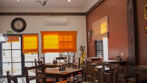 A restaurant interior with wooden tables and chairs, a wall clock, and orange window shades. - Hotel de la Fuente (Orange Walk)