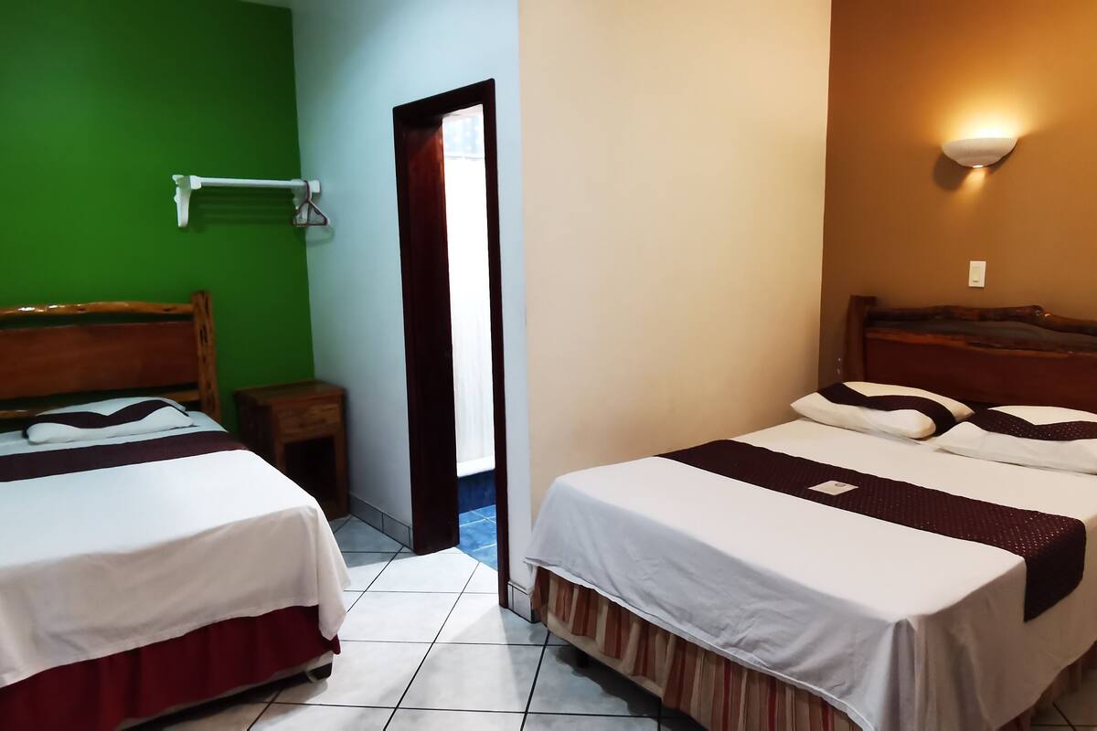 A hotel room with two beds, a wooden headboard, a small wooden table, a wall-mounted towel rack, and a bedside lamp.