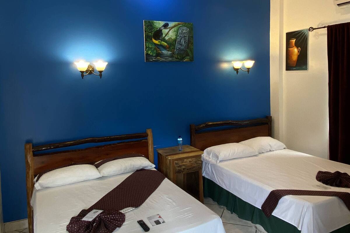 A hotel room with two beds, a painting on the wall, and a water bottle on the nightstand.