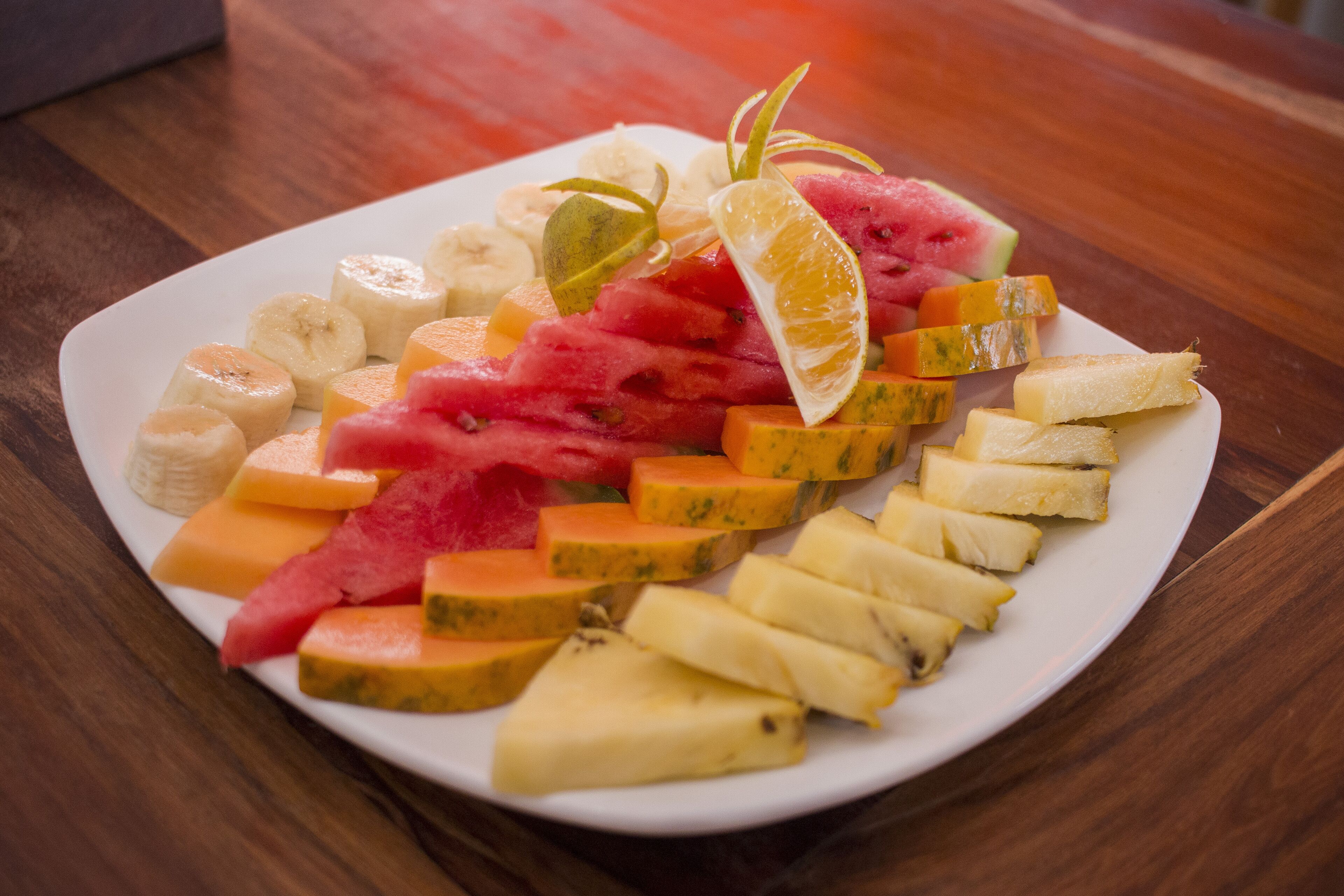 Ein weißer Teller mit verschiedenen Früchten, darunter Wassermelone, Ananas, Banane und Orangenscheiben.