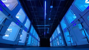 A corridor with multiple rooms, each featuring a large window and a blue light fixture. - Space Night - Hostel (Berlin)