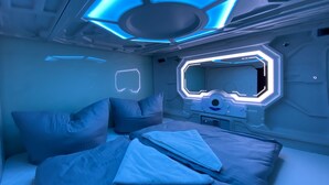 A futuristic room with a bed, pillows, and a control panel. - Space Night - Hostel (Berlin)