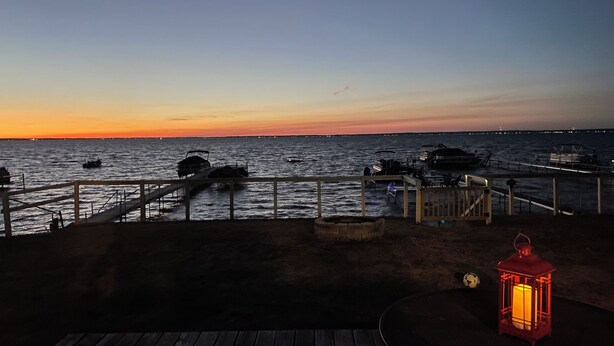 A wooden deck overlooking a marina at sunset with boats docked and a lantern on the right.