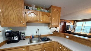 A compact kitchen with wooden cabinets, a coffee maker, a sink, and a window with a view of the sea.
