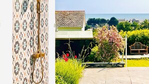 A modern outdoor shower area with patterned tiles, a clear view of the sea, and a pathway leading to a bench. - Seafacing Welsh cottage near the beach with stunning views accommodating 8.  (Pendine)