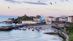 A coastal town with colorful buildings, a harbor with boats, and a lighthouse on a hill. - Seafacing Welsh cottage near the beach with stunning views accommodating 8.  (Pendine)