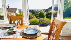 A dining table with a view of the sea and hills, a wooden chair, and a patterned table runner. - Seafacing Welsh cottage near the beach with stunning views accommodating 8.  (Pendine)