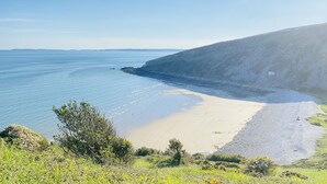 A coastal landscape with a sandy beach, rocky cliffs, and greenery. - Seafacing Welsh cottage near the beach with stunning views accommodating 8.  (Pendine)