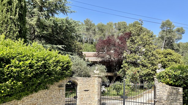 A stone gate with a metal fence, surrounded by lush greenery and trees.