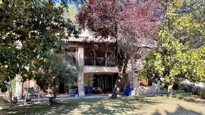 A two-story building with a balcony, surrounded by trees and a grassy lawn.
