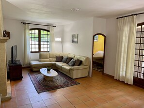 A living room with a beige sectional sofa, a coffee table, a TV on a stand, and a large window with curtains.