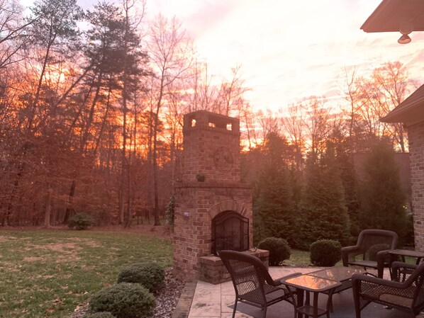 A patio with a stone fireplace, outdoor seating, and a view of trees and sky. - Luxury Home with Office and Man Cave-Ideal for Families, Couples & Market Guests (Summerfield)