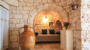 Een kamer met stenen muren, een grote terracotta pot, een bank met kussens en een dressoir.