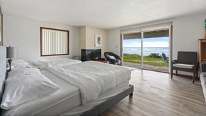 Une chambre avec un grand lit, une télévision et une vue sur la plage, accessible par une porte coulissante.