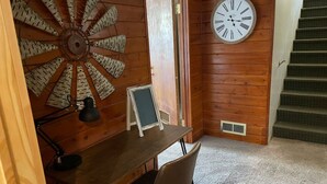 Een kamer met houten lambrisering, een bureau, een klok en een trap.