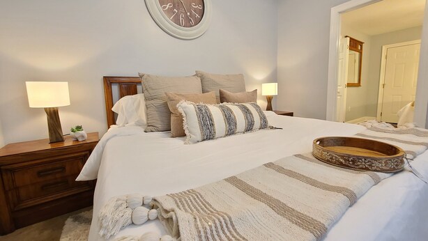 A neatly arranged bedroom with a bed, bedside tables, a wall clock, and a mirror.