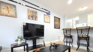 A modern living room with a flat-screen TV, two bar stools, a coffee table, and decorative wall art.