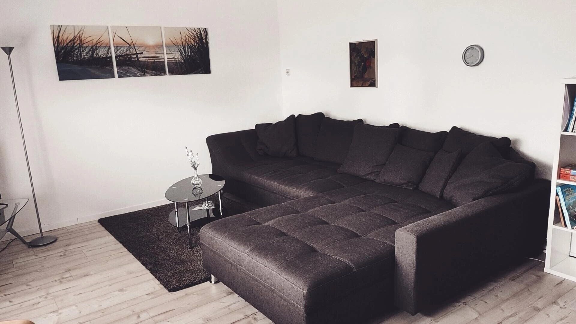 Un salon moderne avec un canapé d’angle gris foncé, une petite table d’appoint sur laquelle est posé un vase, et un lampadaire.