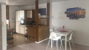 A compact kitchen with a wooden island, a dining area with a white table and chairs, and a wall-mounted painting of a sunset. - Ferienwohnung auf dem Lande (Twedt)