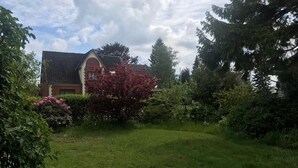 A house with a sloped roof, surrounded by a well-maintained garden with various shrubs and flowering plants. - Ferienwohnung auf dem Lande (Twedt)