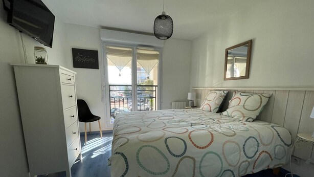 Un dormitorio con cama, cómoda, silla, escritorio, espejo y balcón con vistas.