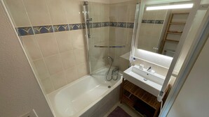Un baño con bañera, cabina de ducha de vidrio, lavamanos con espejo y piso de baldosas.