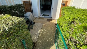 Un patio con un área de estar cubierta al aire libre, una puerta de madera y la entrada de un edificio con un cartel de número.