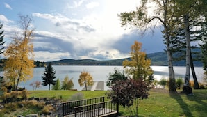 A lakeside park with a wooden deck, a small bridge, and a view of a calm lake with mountains in the background. - Lakefront Property- Newly Updated Four Bedroom House, Sleeps 10 (Whitefish)