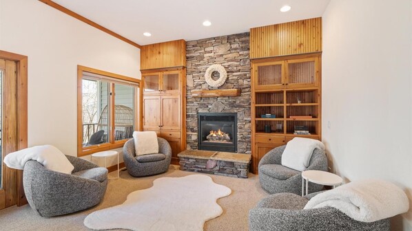 A cozy living room with a stone fireplace, wooden bookshelves, and comfortable seating.