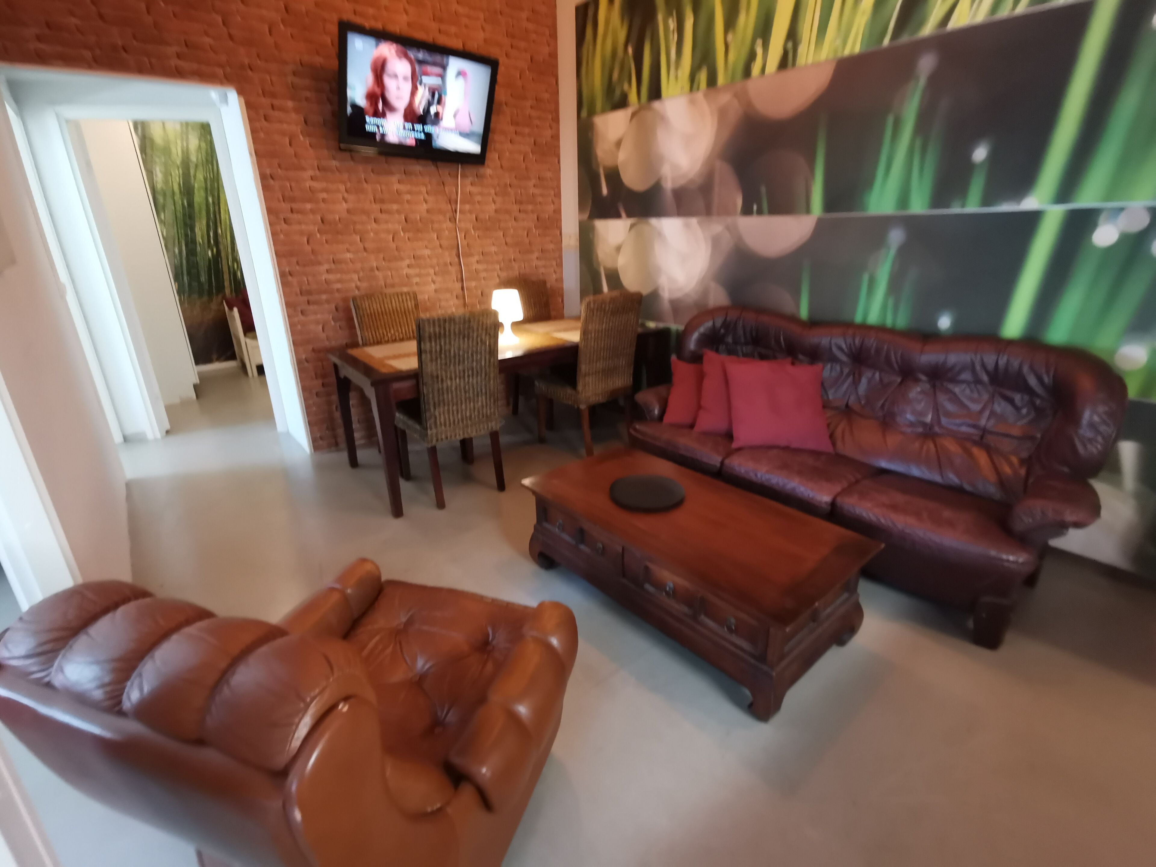 Una sala de estar con un sofá de cuero, una mesa de centro de madera y un televisor montado en una pared de ladrillo.