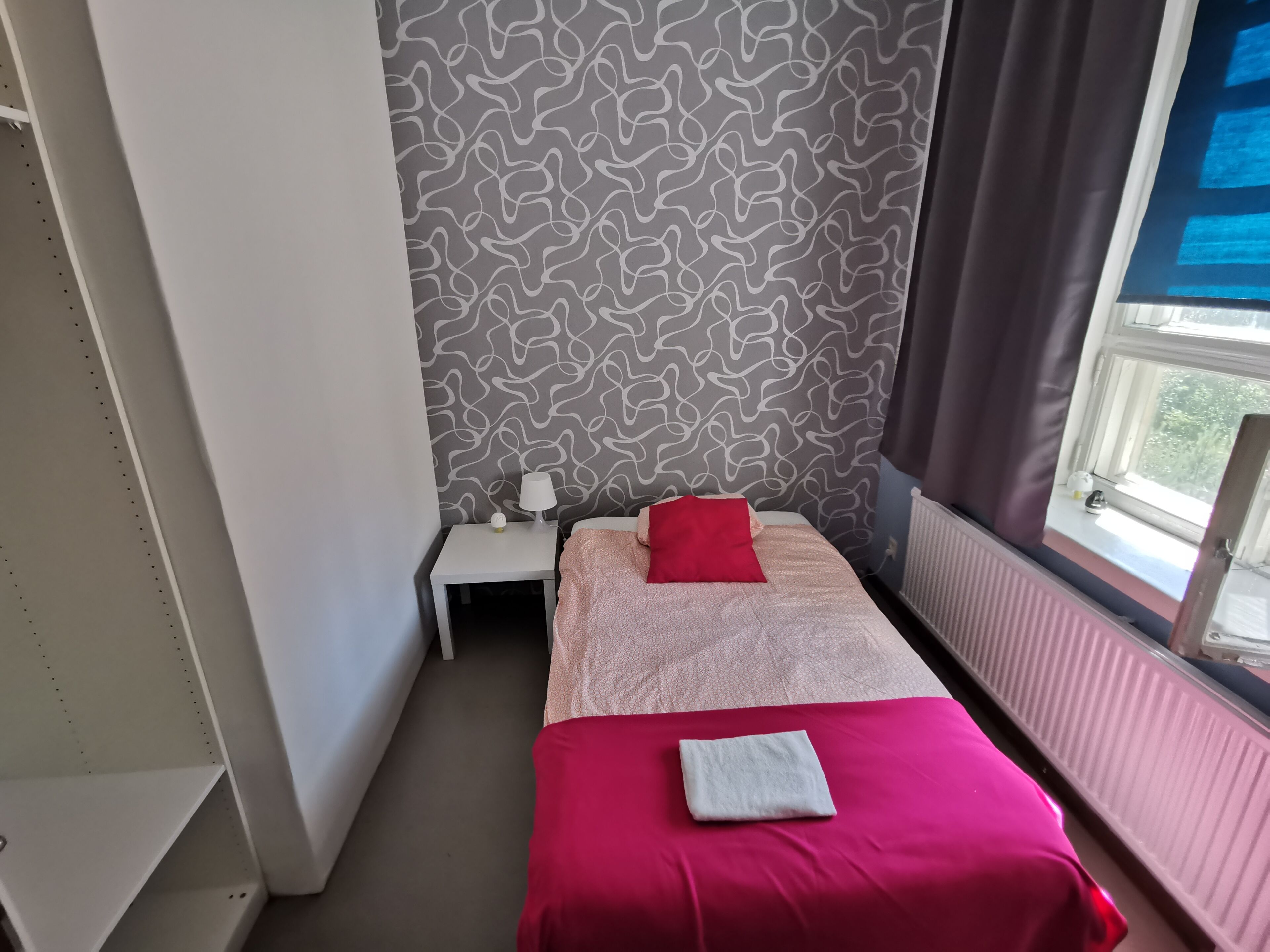 Une chambre avec deux lits, une table de chevet, une fenêtre avec des rideaux et un mur décoré d’un motif.