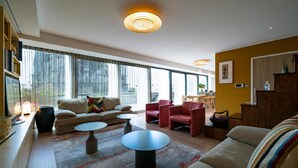 A modern living room with a sofa, armchairs, and a coffee table. There are large windows with a view of the city. - 4 Private Homes for rent to live the sparkling Remoise life. (Reims)