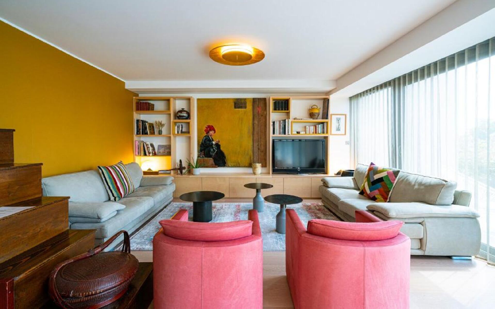 Una sala de estar moderna con un sofá, dos otomanas rosas, una mesa de centro y un televisor.