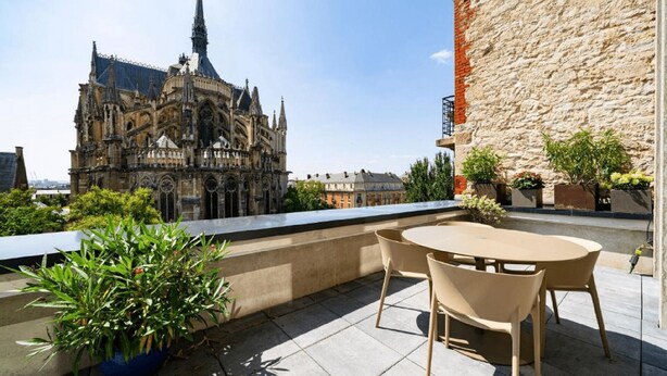 A rooftop terrace with a view of a historic cathedral, a stone wall, and potted plants. - 4 Private Homes for rent to live the sparkling Remoise life. (Reims)