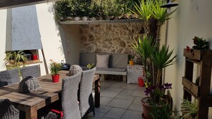 Une terrasse extérieure avec un mur en pierre, des meubles en osier et diverses plantes en pot.