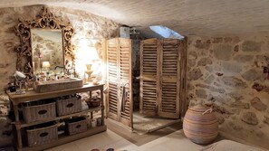 Une salle de bain rustique avec des murs en pierre, un meuble-lavabo en bois, un miroir doté d’un cadre orné et un grand panier tressé.