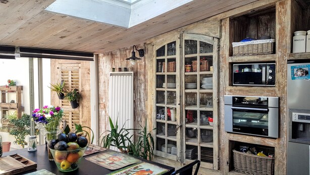 A rustic kitchen with wooden beams, a dining area with a table set for two, and a built-in oven. - Maison de Village Atypique (Vidauban)