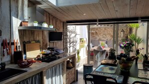 A rustic kitchen with a wooden countertop, a gas stove, and a variety of kitchen utensils. There is a dining area with wicker chairs and a table set for two. - Maison de Village Atypique (Vidauban)