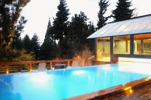 A modern house with a glass conservatory, a swimming pool, and a wooden deck. - 1BR Luxury Condos Aldea Andina (San Carlos de Bariloche)